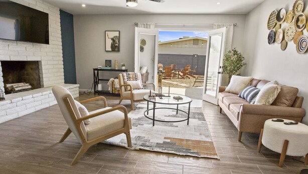 A spacious living room with a fireplace, a coffee table, and a sofa. There is a door leading to an outdoor patio area.