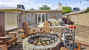 A backyard with a stone fire pit, wooden chairs, and a table.