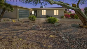 A modern two-story house with a garage, surrounded by a landscaped garden with rocks and shrubs.
