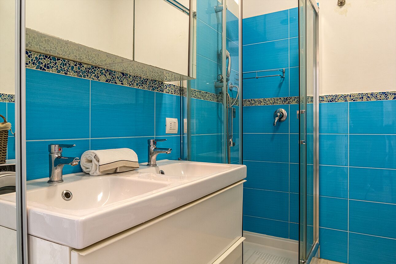 A bathroom with a white sink, a glass shower enclosure, and blue tiled walls.