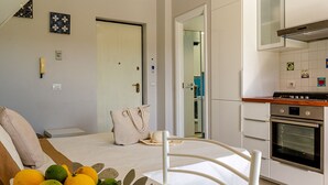 A modern kitchen with white cabinets, a stove, and a dining area with a white chair and table. - Perla Marina-Giardini Naxos (Giardini Naxos)