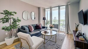 Een moderne woonkamer met een bank, fauteuil, salontafel en een groot raam met gordijnen.