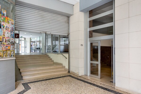 Un interior moderno con una escalera que sube a un segundo piso, una entrada con puerta de vidrio y suelo de baldosas.