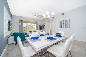 Comedor moderno con una mesa blanca para seis personas, sillas color aguamarina y una araña.