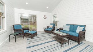 Un patio techado con mobiliario de mimbre, una mesa de centro de vidrio y una alfombra a rayas.