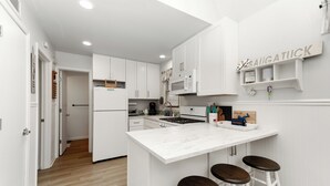 Una cocina moderna con armarios blancos, una isla central con taburetes, un microondas y una estufa.
