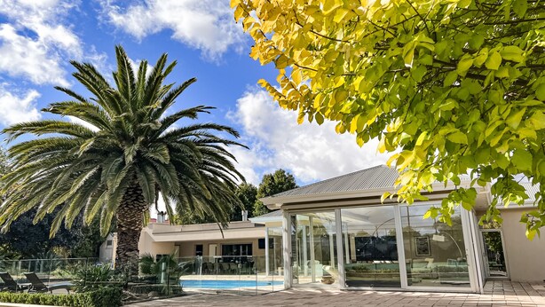 A modern house with a glass-enclosed patio, a swimming pool, and a large palm tree. - Tanunda House - Luxury 5 BR in Barossa Wine Region (Tanunda)