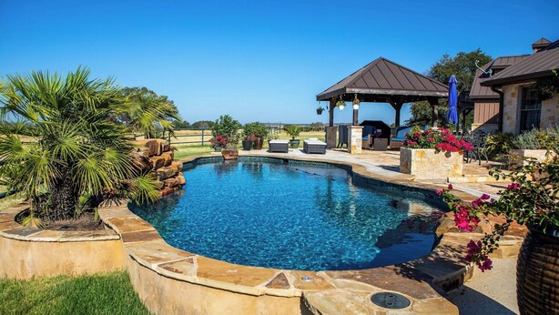 A swimming pool with a stone border, a gazebo, and outdoor furniture.