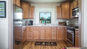 A kitchen with wooden cabinets, stainless steel appliances, a window with a view, and a rug on the floor.