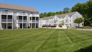A row of two-story townhouses with balconies, a well-maintained lawn, and parked cars. - Rehoboth Beach Townhouse Pool Parking Porch (Rehoboth Beach)