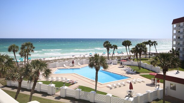 Een zwembadgedeelte van een resort met uitzicht op het strand en de oceaan, omringd door palmbomen en ligbedden.