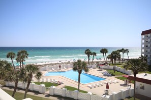 Área de piscina en un resort con vista a la playa y al océano, rodeada de palmeras y sillas de descanso.