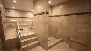Een wellnessruimte met een jacuzzi, marmeren wanden en een douche met glazen wanden.