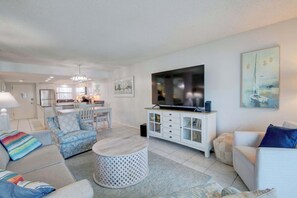 Una sala de estar moderna con televisión, sofá, sillones, comedor y cocina.