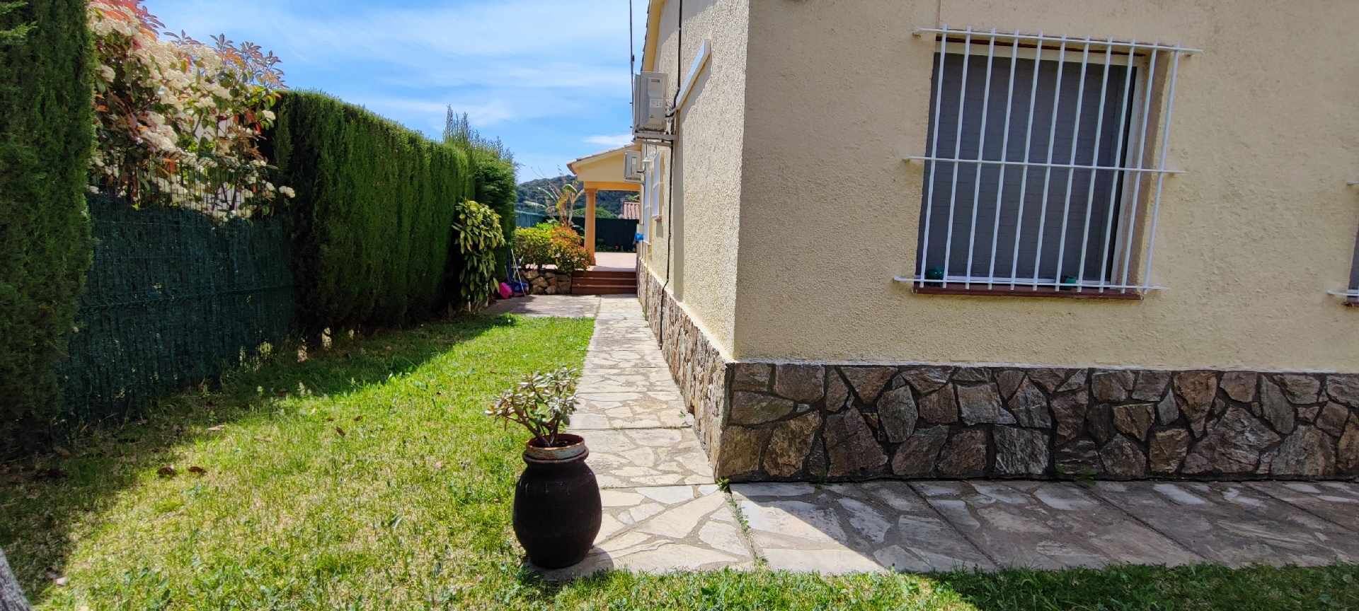 A pathway leading to a building with a stone base and a window with bars.