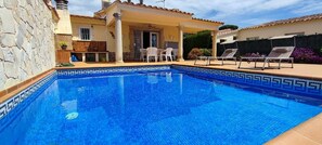 A swimming pool with a tiled edge, a covered patio area with chairs, and a stone wall. - Villa Cecilia, an oasis on the Costa Brava (S'Agaro)