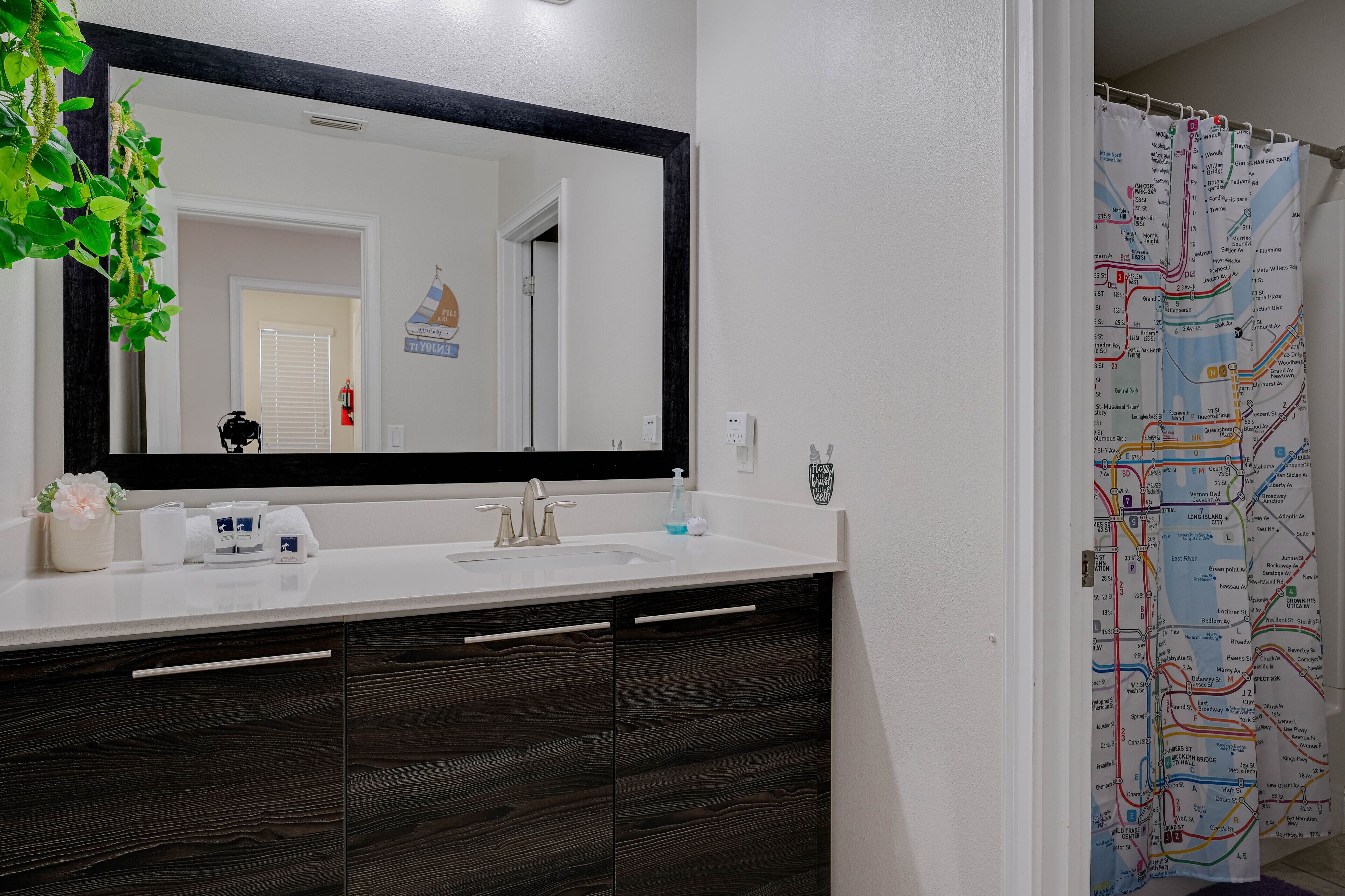 Une salle de bain avec un grand miroir, des meubles en bois foncé, un lavabo blanc et une carte accrochée au mur.