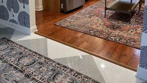 Una cocina moderna con armarios de madera, un refrigerador de acero inoxidable, una mesa de comedor con sillas y una alfombra estampada.
