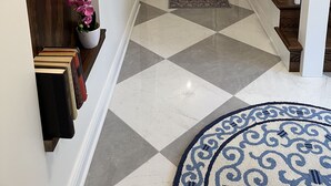 Un pasillo con piso a cuadros, una escalera de madera con barandilla blanca y una orquídea en maceta.