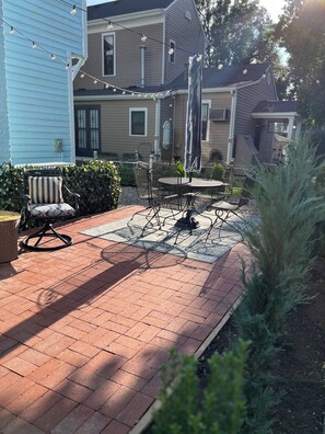 Un patio con una mesa y sillas de metal, una silla de mimbre y luces colgantes.