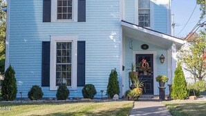 Una casa de dos plantas en azul claro con contraventanas oscuras, un porche y un cartel con el número 112.
