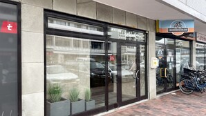 Facciata di un edificio con ampie vetrate, un'insegna per 'Fahrradverleih' e un'area di parcheggio per biciclette.