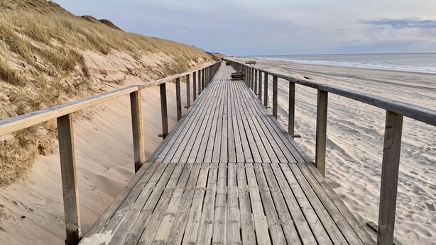 Una passerella di legno che conduce a una spiaggia, con dune da un lato e l'oceano dall'altro.