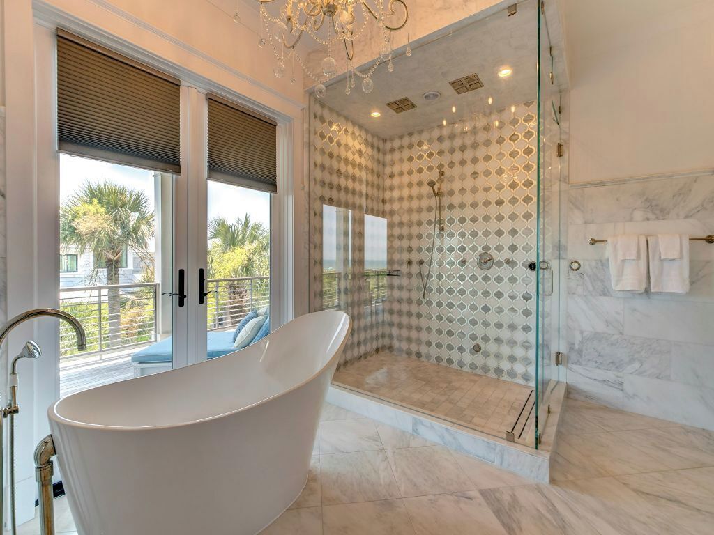 Een moderne badkamer met een vrijstaand bad, een douche met glazen wanden en uitzicht op palmbomen.