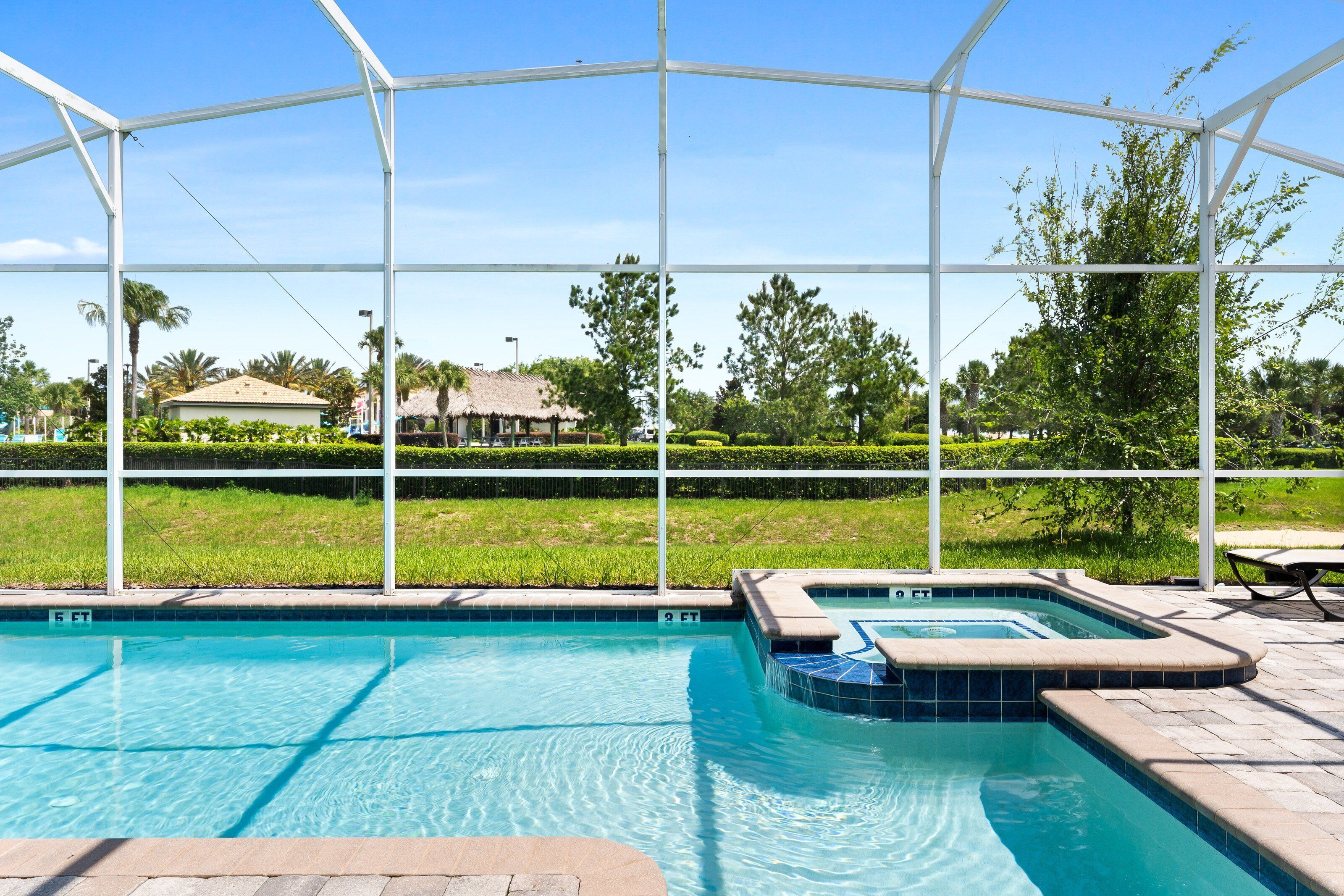 Una piscina con hidromasaje, rodeada por una cubierta blanca y vistas a un área verde con árboles y un edificio al fondo.