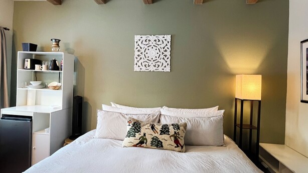 Une chambre à coucher bien rangée, avec un lit, des oreillers, une table de chevet, une lampe et une étagère contenant divers objets.