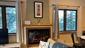 Una sala de estar acogedora con chimenea, un cuadro en la pared y un ventanal con cortinas.