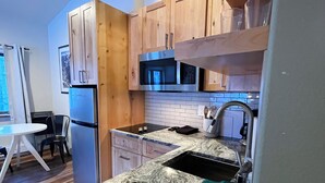 Una cocina moderna con armarios de madera, un refrigerador de acero inoxidable, un microondas y una encimera de granito.
