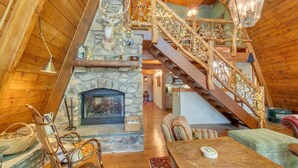 A cozy cabin interior with a stone fireplace, wooden staircase, and rustic decor.