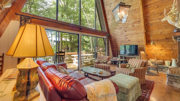 A spacious loft-style living room with a large window, leather sofa, striped armchairs, and a flat-screen TV.