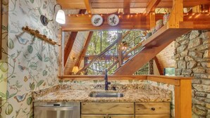 A rustic kitchen with a stone wall, wooden beams, and a wooden countertop.