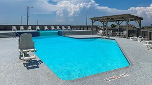 En swimmingpool med klart, blåt vand, omgivet af liggestole og en træpavillon.