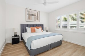 A bedroom with a bed, nightstands, a ceiling fan, a window with blinds, and a framed picture on the wall. - Urban Rest Neutral Bay Apartments (Neutral Bay)