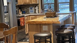 A kitchen with wooden cabinets, a stainless steel refrigerator, a granite countertop, and a large window with a view of trees. - Cozy Lakefront Cottage on Little Pequaywan ~ Great for all seasons (Duluth)