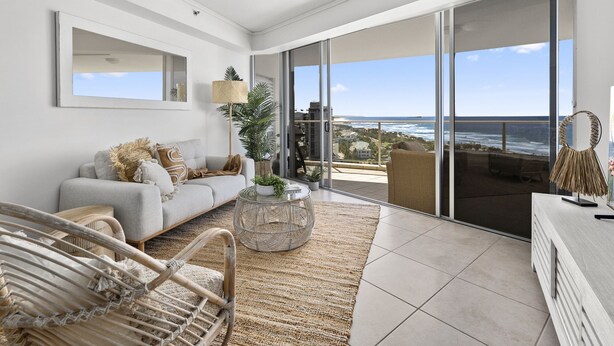 A spacious balcony with a view of the ocean, a grey sofa, wicker chairs, and a round coffee table.