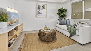 A modern living room with a flat-screen TV, a framed picture, a large potted plant, a white sofa, and a round coffee table.