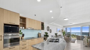 A modern kitchen with built-in appliances, a large island with a sink, and a view of the ocean through large windows.