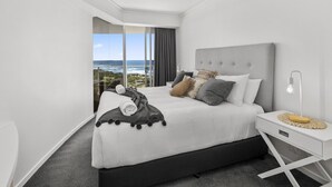 A modern hotel room with a large bed, a bedside table with a lamp, and a view of the ocean.