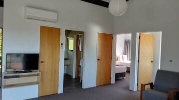 A spacious living area with a flat-screen TV, a grey sofa, and wooden doors leading to other rooms.