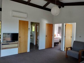 A spacious living area with a flat-screen TV, a grey sofa, and wooden doors leading to other rooms. - Two Bedroom Apartment Sea View (Kaiteriteri)