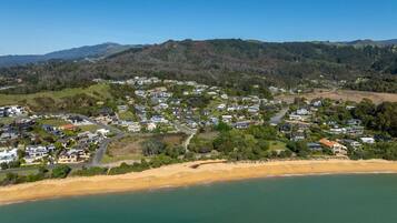 A coastal residential area with houses, a beach, and hills in the background.