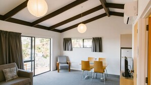 A modern room with a sofa, dining table, chairs, and a TV. - Two Bedroom Apartment Sea View (Kaiteriteri)