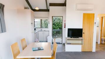 A modern room with a dining table, chairs, a television, and a kitchen area visible through an open door.