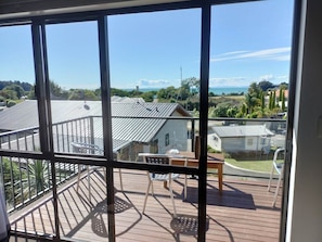 A balcony with a table and chairs, overlooking a residential area with houses and a clear sky. - Two Bedroom Apartment Sea View unit 8 (Kaiteriteri)