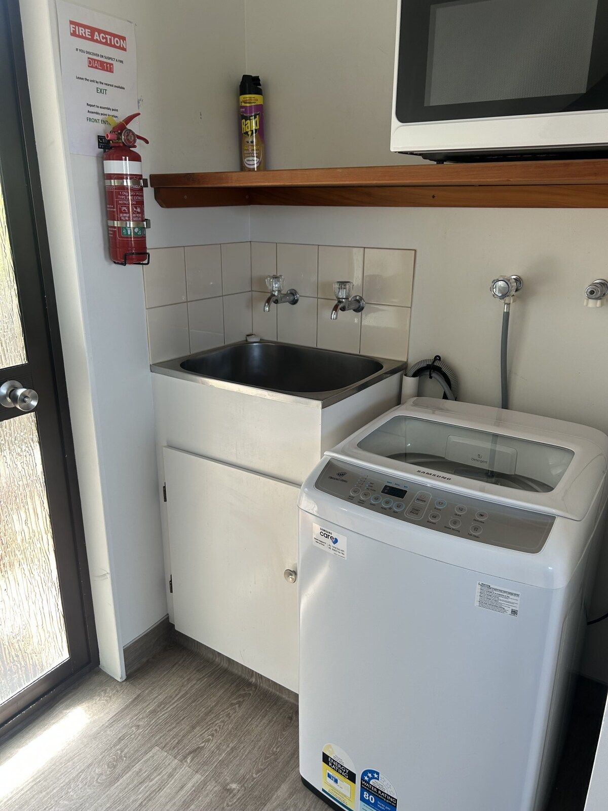 A kitchen with a sink, a white washing machine, a fire extinguisher, and a fire action notice.