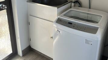 A kitchen with a sink, a white washing machine, a fire extinguisher, and a fire action notice.